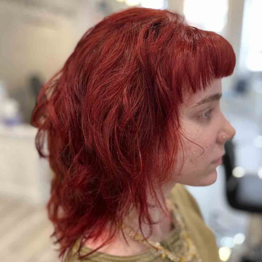 Side post of a girl with short tousled red wolf cut with blunt micro bangs