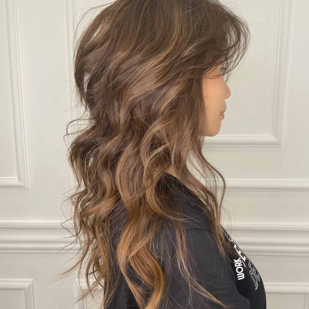 Side pose of a girl with a wavy wolf cut with balayage highlights