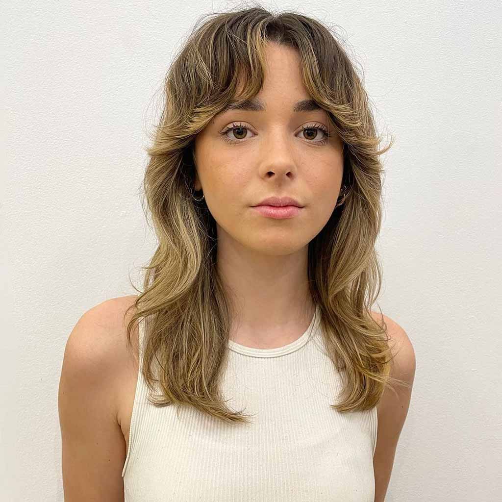 a girl with a balayage wolf cut and curtain bangs wearing a tank top