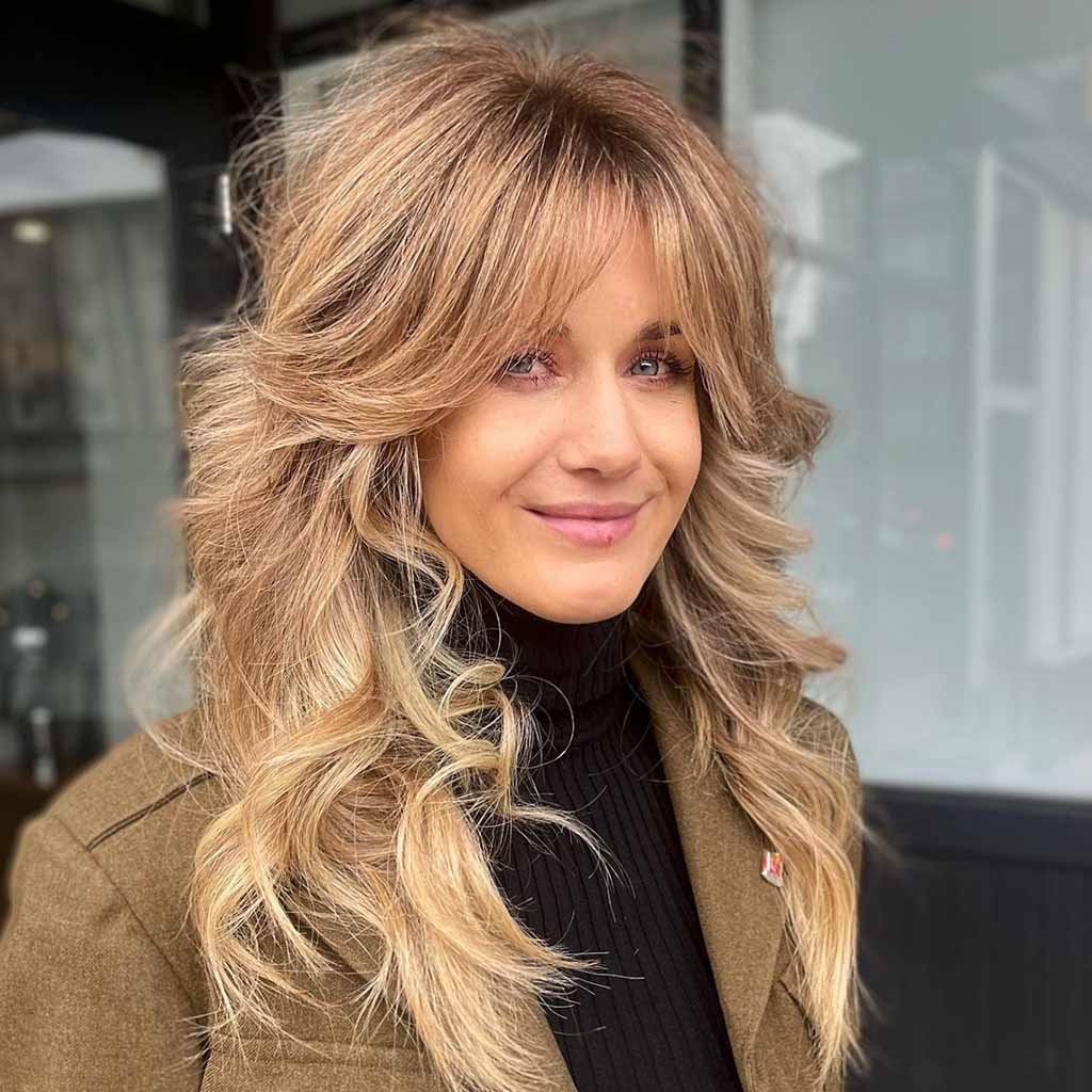 a girl with lovely balayage hair smiling at the camera, wearing a jacket and a high neck
