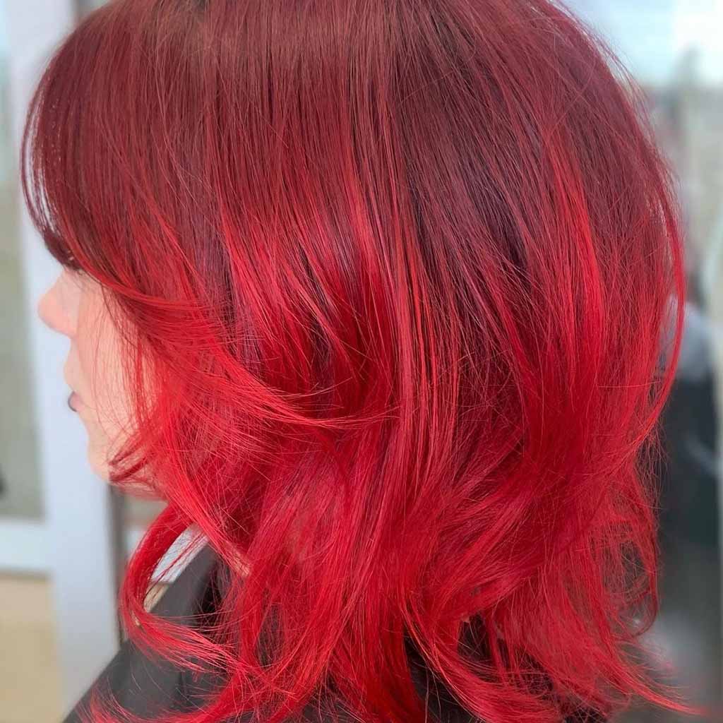 Side pose of a girl with red extended bob wolf cut, wearing black barber's cover 