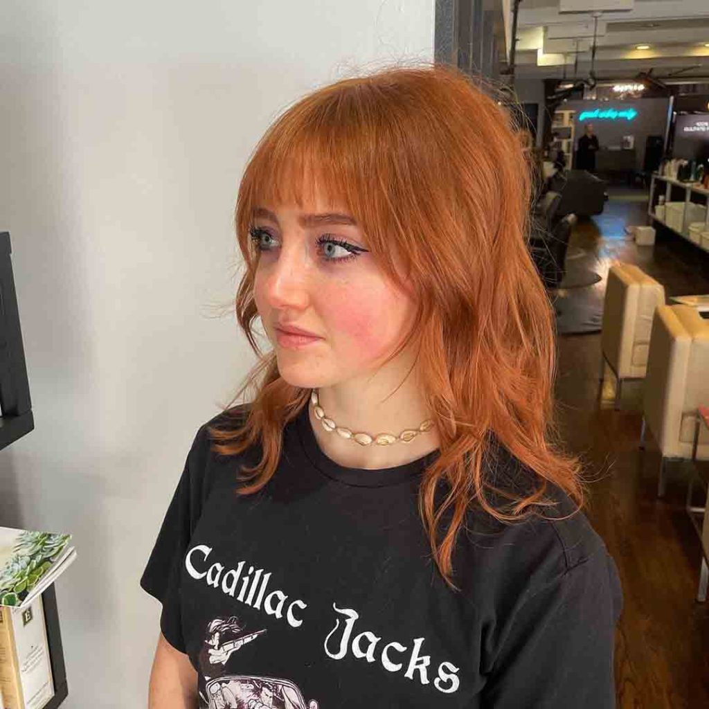 a ginger shaggy wolf cut hair girl with green eyes wearing a neck chain and printed black tshirt