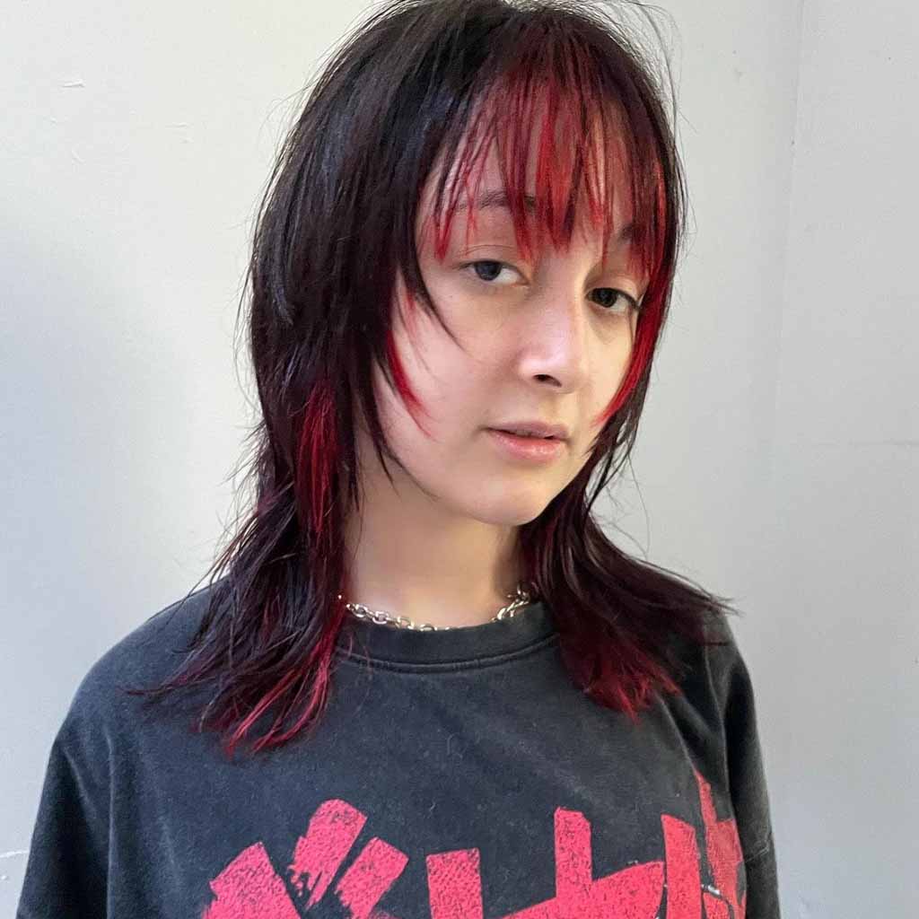 A girl with straight medium wolf cut and extended choppy red bangs, wearing a black printed tshirt