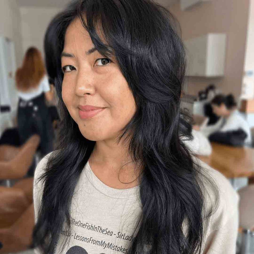 a woman with jet black hair and black shaggy wolf cut, smiling at the camera