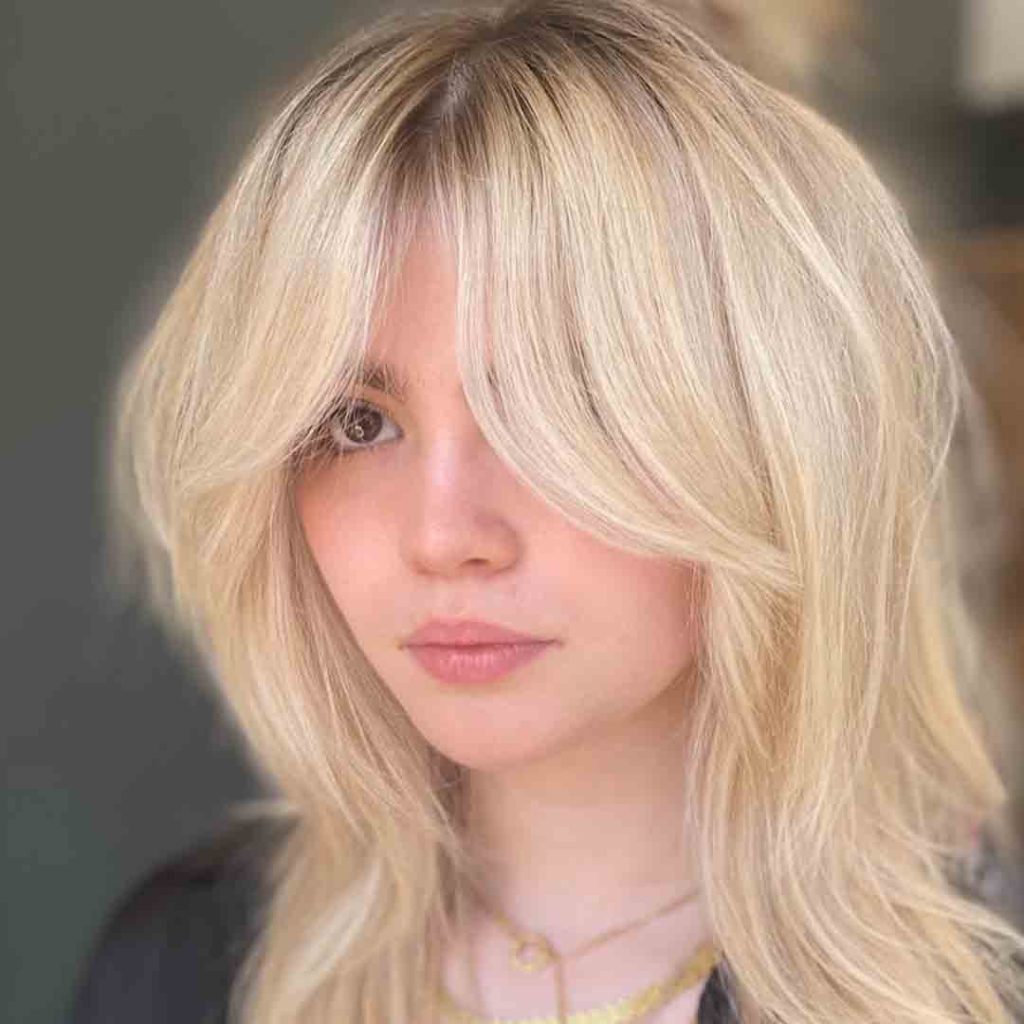 A girl ⁢with blonde wolf cut with⁤ wavy bottleneck bangs, ⁢wearing two neck chains and a black top