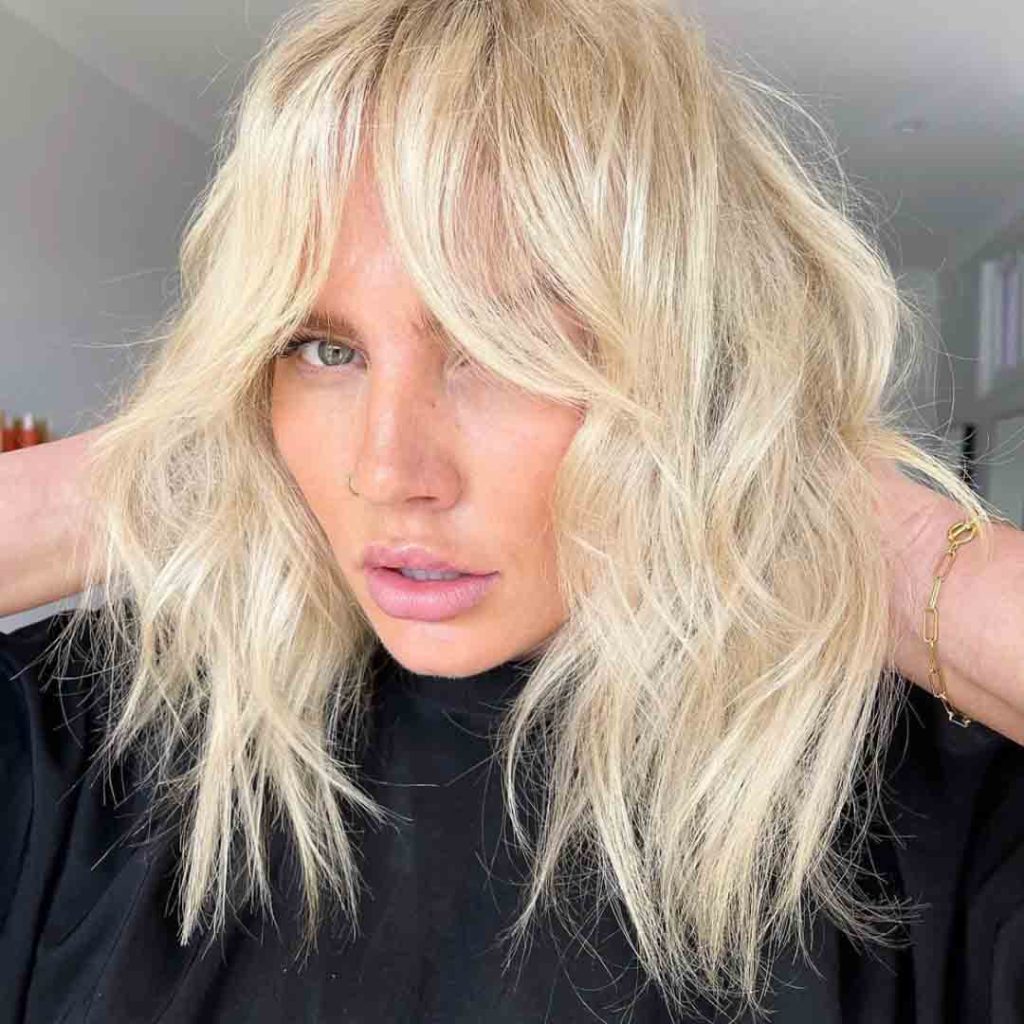 a blonde girl with green eyes and blonde shaggy wolf cut posing for the camera in a black top